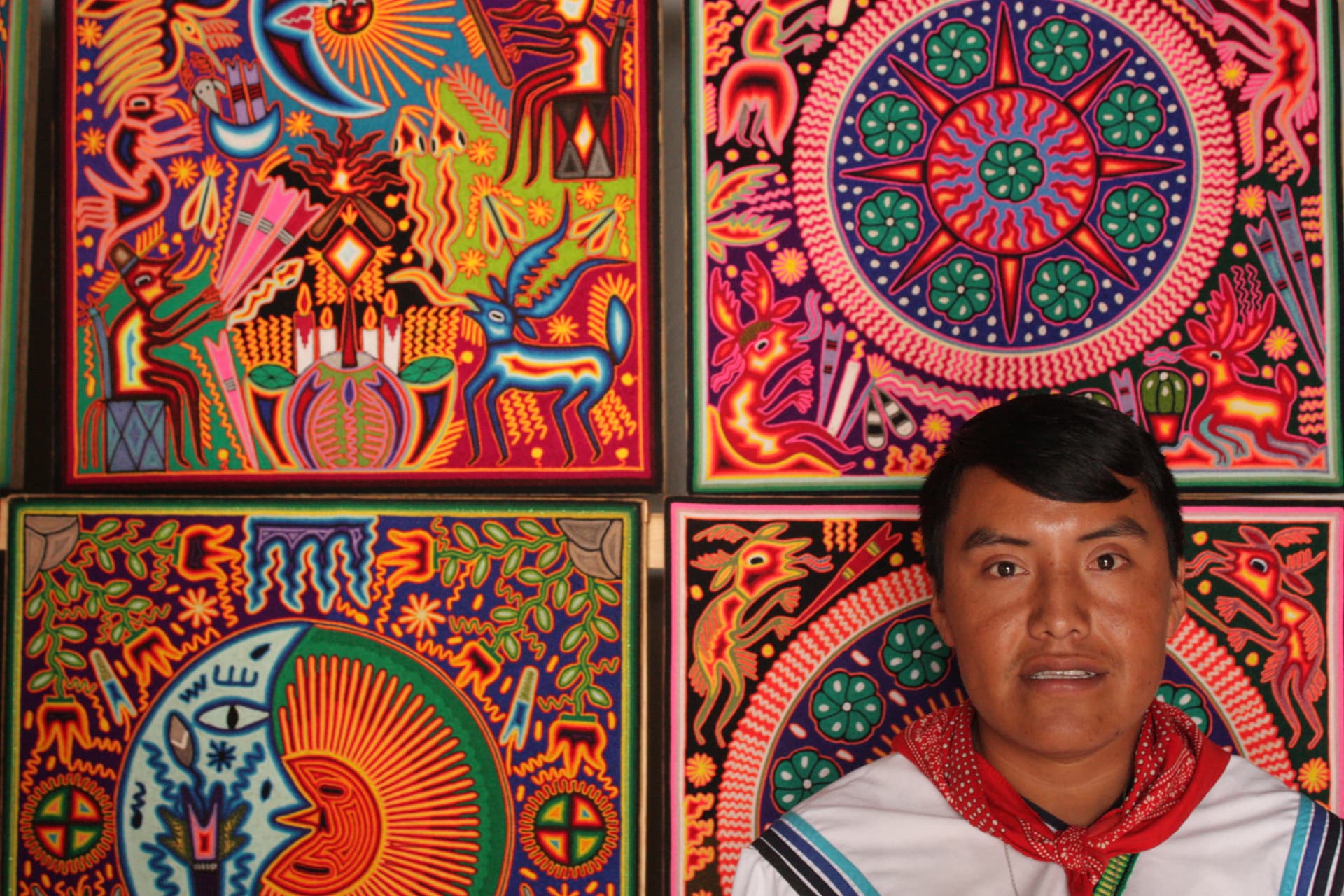 Artista wixárika frente a sus cuadros de estambre