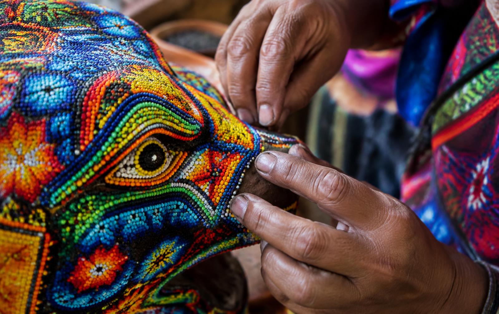 Manos de artista wixárika colocando chaquira